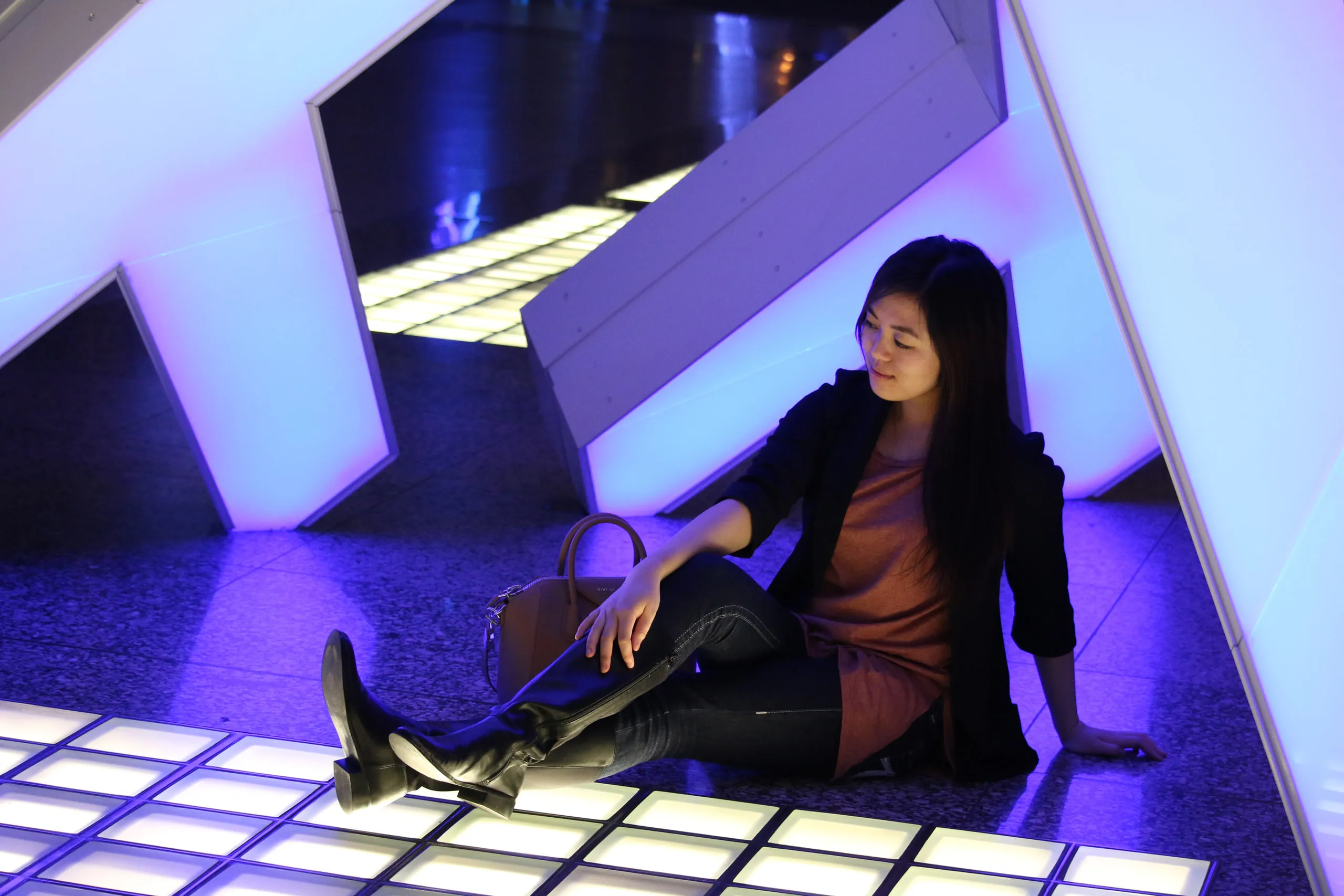 A woman sits among angular walls and glowing blue floor panels.