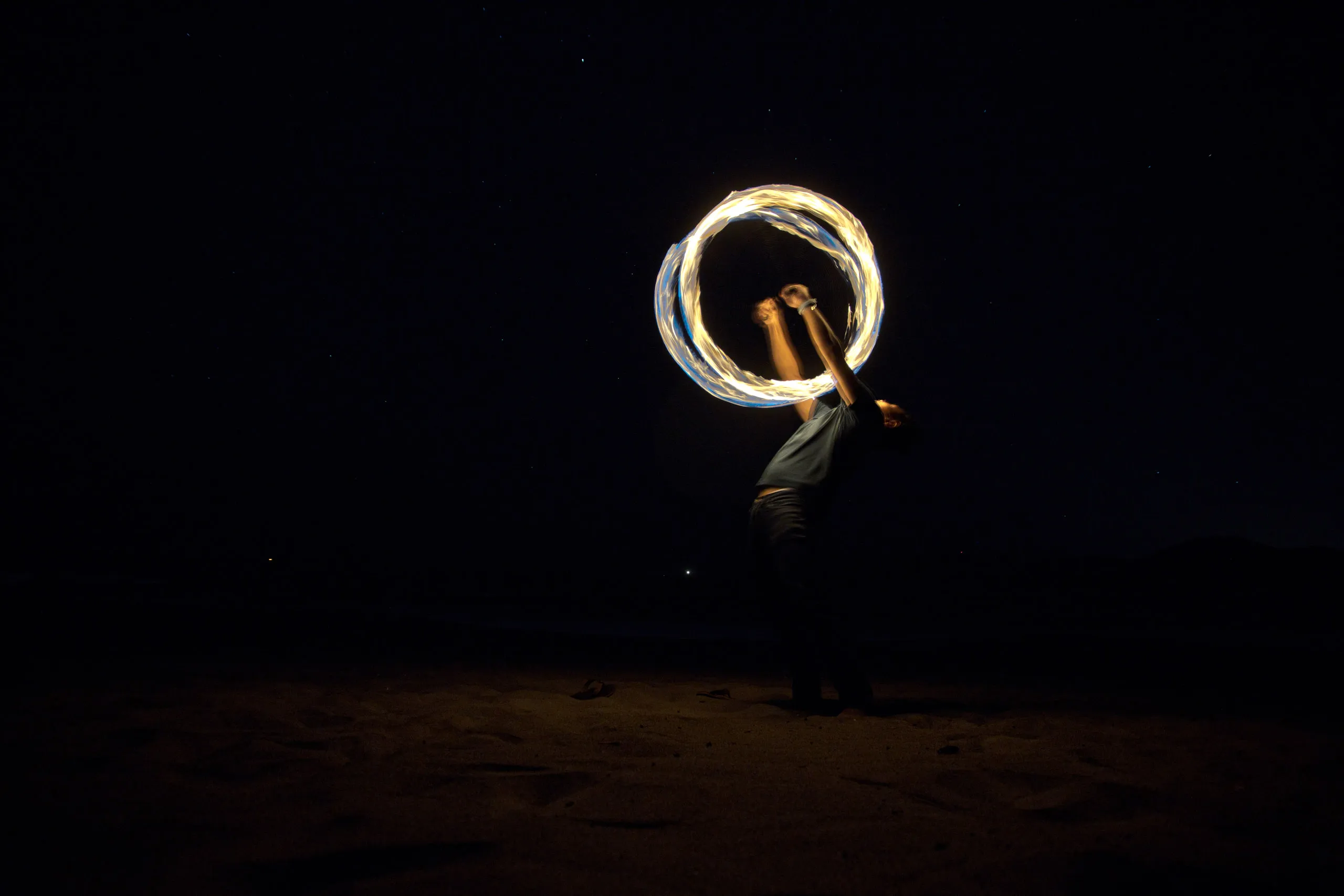 A fire performer holds a glowing ring of light against the night sky.