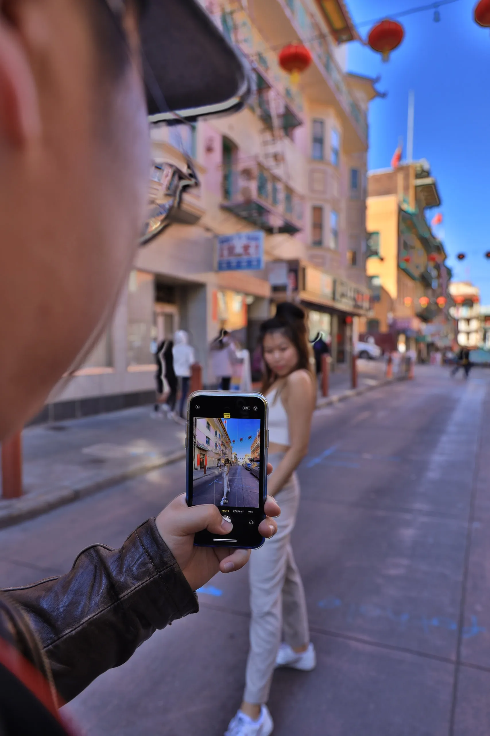 A photographer frames a woman on a lantern-lined city street through a phone.