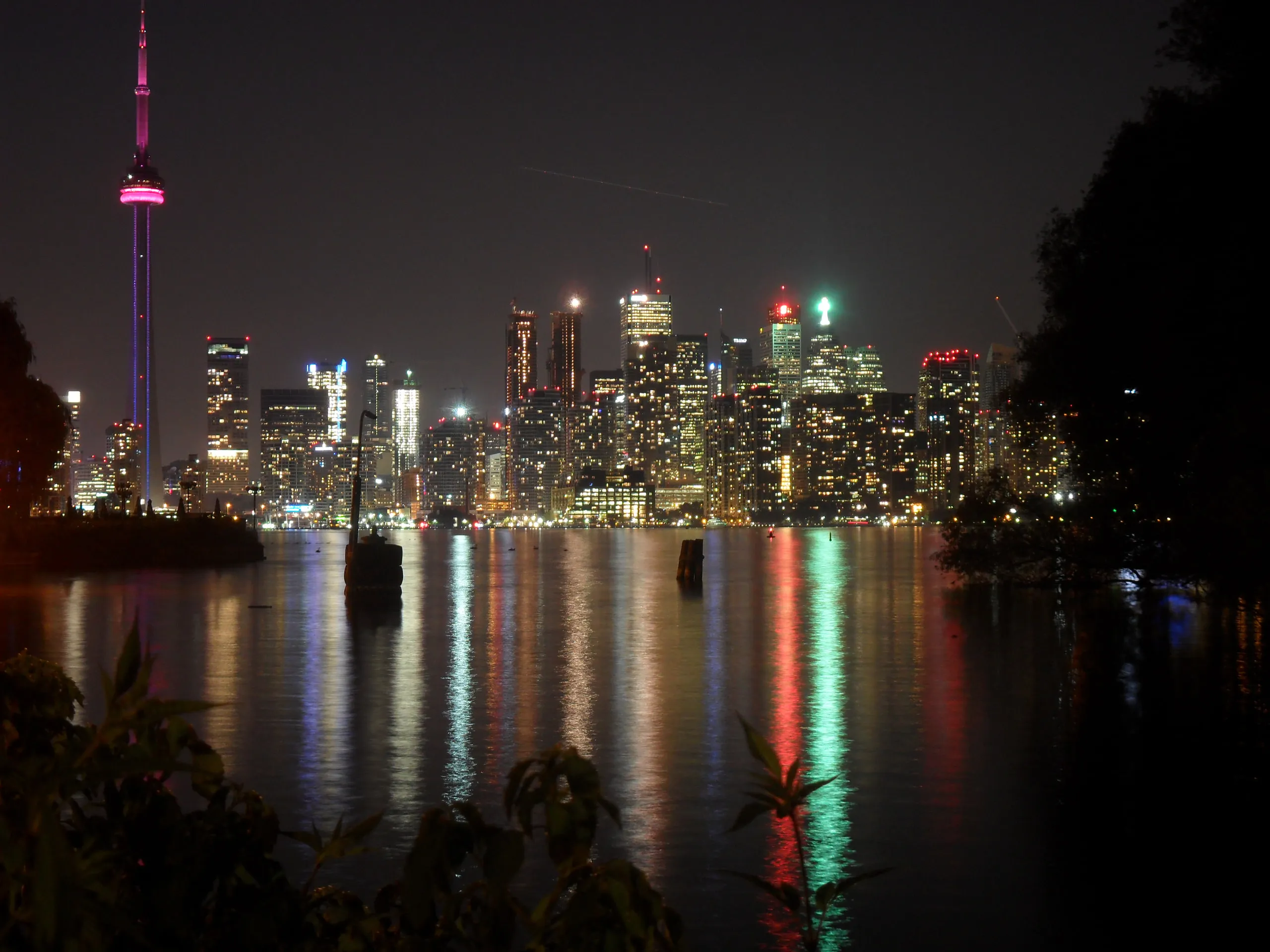 The Toronto skyline and CN Tower reflect across the harbour at night.